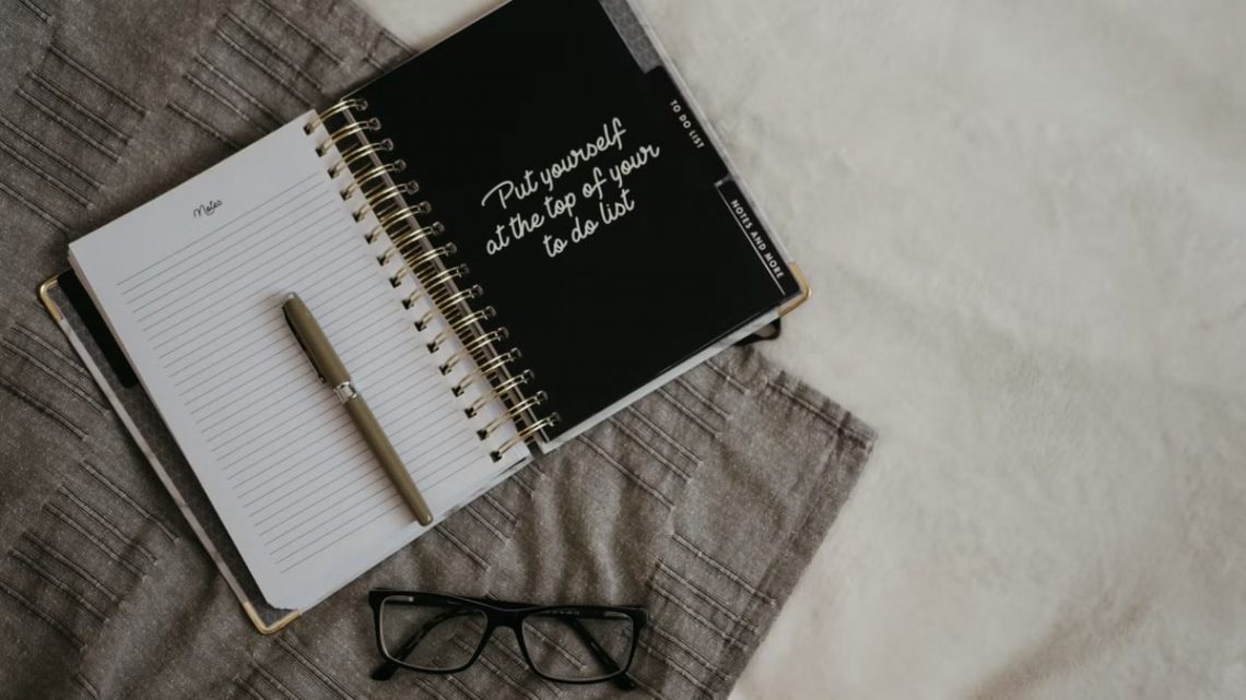 Stylish flatlay featuring a planner with quote, pen, and eyeglasses on a neutral background.